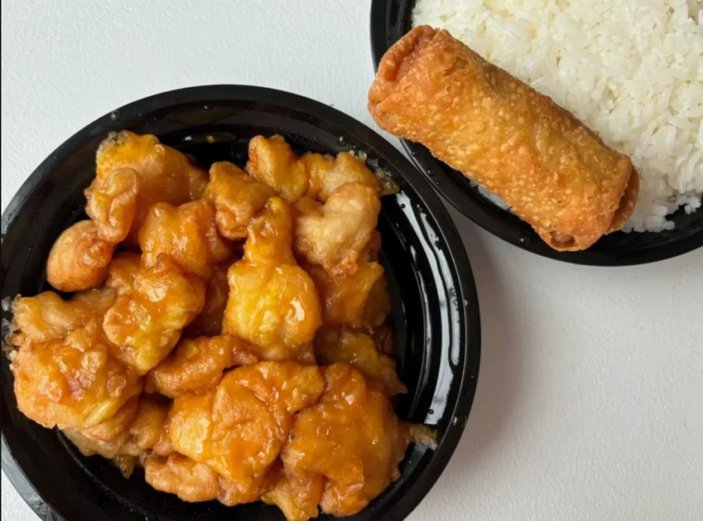 "Champaign Chinese sweet and sour chicken beautifully plated with vibrant colors, served with steamed rice and chopsticks on a wooden dining table."